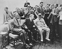 Franklin D. Roosevelt, le Premier ministre canadien William Lyon Mackenzie King, et Winston Churchill, assis au premier plan, lors de la conférence de Québec. Des hommes se tiennent debout à l'arrière-plan.