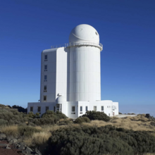 The image shows a large tower housing telescope dome on it's top floor. The dome has a small hole in it where the telescope looks out.