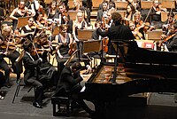 A concert pianist playing a piano concerto with a full orchestra. Orchestras are one of the largest musical ensembles, as they can contain as many as 100 musicians. In the 2010s, most orchestras receive income from ticket sales, donations and government funding. The latter two sources of income are required because ticket sales alone do not provide enough income for most groups. 100th 2.jpg