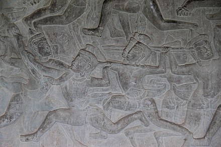 A fight scene on an Angkor Wat bas-relief mural. A man uses an elbow strike to the jaw of his opponent while enemies with spears approach.
