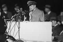 MacArthur, in uniform, speaks from a rostrum with several microphones.