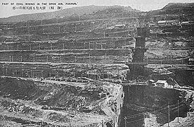 Photo d'un flanc de colline éventré par une mine à ciel ouvert. Des strates régulières coupent horizontalement le sol.