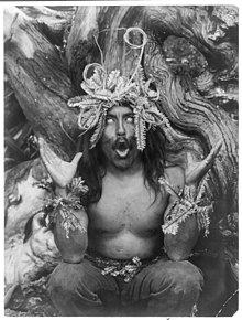 Hamatsa Shaman seated on the ground in front of a tree, facing front, possessed by supernatural power after having spent several days in the woods as part of an initiation ritual Hamatsa shaman.jpg