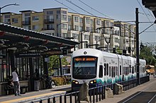 Light rail vehicle at ground level platform. Behind it is a multi-story apartment building