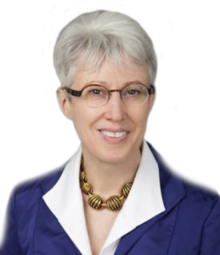 A photographic portrait of a middle-aged woman from the shoulders up, wearing a suit and eyeglasses