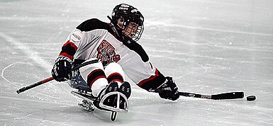 An ice sledge hockey player reaches for the puck Sled hockey player.jpg