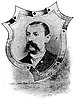 Head of a white man with a drooping mustache and short hair, wearing a dark suit over a light-colored shirt and tie. The portrait is surrounded by a shield-shaped decorative frame.