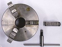 Self-centering three-jaw chuck and key with one jaw removed and inverted showing the teeth that engage in the scroll plate. The scroll plate is rotated within the chuck body by the key, the scroll engages the teeth on the underside of the jaws which moves the three jaws in unison, to tighten or release the workpiece. ThreeJawChuckKey.jpg