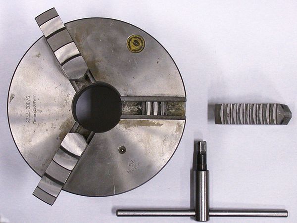 Self-centering three-jaw chuck and key with one jaw removed and inverted showing the teeth that engage in the scroll plate. The scroll plate is rotate