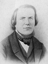 Head and bust of a man with a high forehead, hair reaching his shoulders, wearing a 19th-century three-piece suit and a cravat.