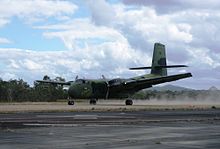 Colour photograph of a camouflage painted aircraft driving along a dirt airstrip