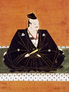 La daimyō Azai Nagamasa vêtu de noir et assis en tailleur.