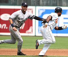 Jeter in a grey baseball uniform tags his glove to a baserunner from the opposing team.