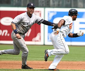 Jeter in a grey baseball uniform tags his glove to a baserunner from the opposing team.