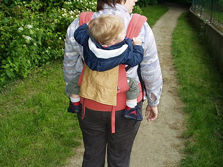 Woman wears an ERGO Baby brand baby carrier on her back Ergobabycarrier.jpg