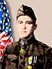 Head and shoulders of a young man in a brown military uniform with a garrison cap. A medal hangs down from his neck, the strap laying under his collar, and two medals hang from colorful ribbons on his chest.