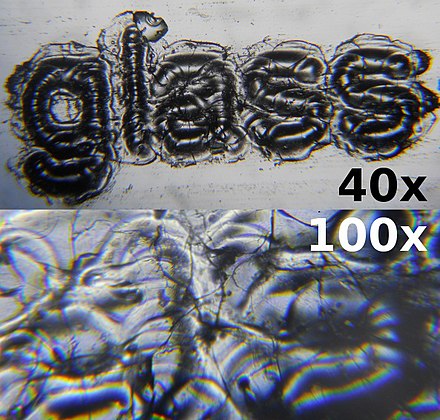 Laser engraved glass microscope slide with the word "glass" engraved in 3pt font. Magnified to 40x and 100x