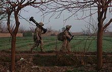 soldiers walk along field with carrying large weapons