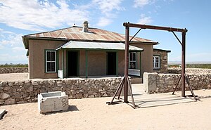 Single-storey building in a desert landscape with a corrugated metal roof. And a veranda