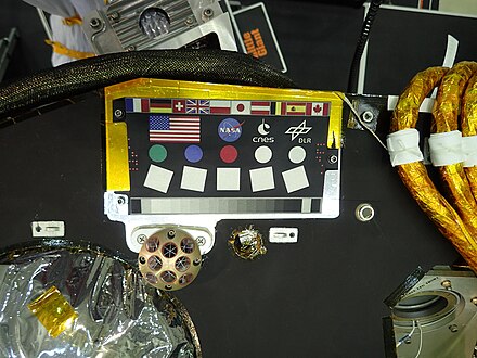 Sur cette photo du plateau supérieur de l'atterrisseur sont visibles les drapeaux des pays et sigles des agences spatiales contributeurs de la mission, les mires (ronds colorés) utilisées pour étalonner les couleurs de la caméra, le rétroréflecteur LaRRI en coins de cube (en bas à gauche) et à droite de ce dernier, une des deux puces contenant les noms des participants à la campagne « envoyez votre nom sur Mars ».