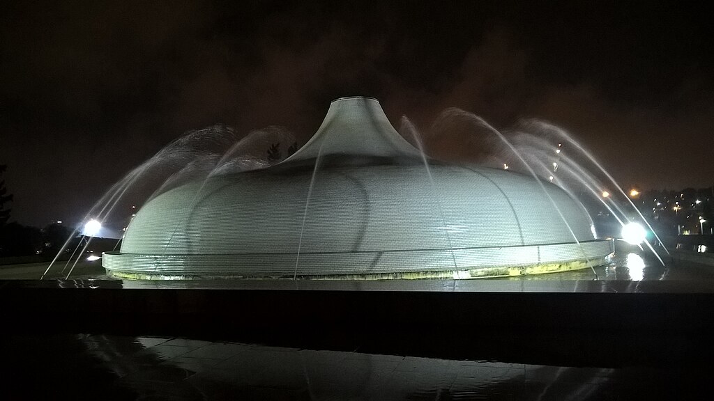 a large domed building at night surrounded by fountains