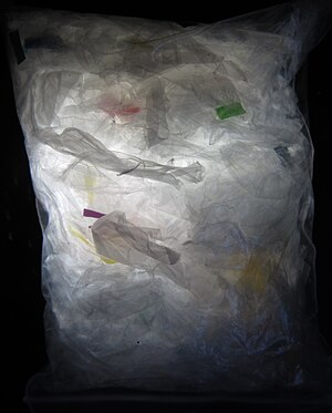 Photo of transparent plastic pouch filled mostly with transparent or semi-transparent pieces of fabric-like plastic material, with light being shone from the underside into the pouch—looks like an X ray, doesn’t it?