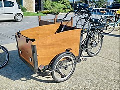 Un vélo triporteur à assistance électrique avec des sièges pour enfants aménagés dans la caisse en bois.