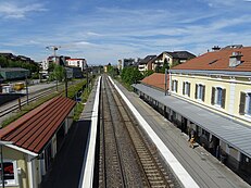 Hinterleuchteter Blick von einer Fußgängerbrücke auf die Gleise und das Fahrgastgebäude.