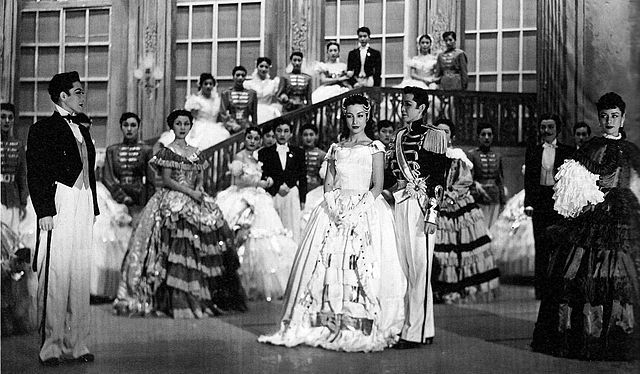 A historical photograph of a stage performance; all of the actors are women, some of whom are cross-dressing.