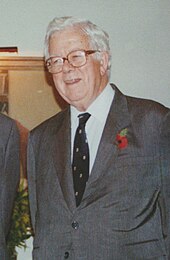 A white-haired man in a grey suit and tie