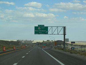 gantry sign stating "Exit 410—US-93 Alt—West Wendover—Ely" as a freeway descends into a town with salt flats in the background.