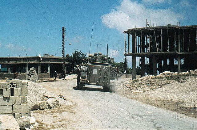 נגמ"ש צה"ל בדרום לבנון, 1982 - רכב צבאי הנוסע על זחלים, בכביש צר מישורי, בין אתרי בנייה.