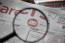 Zvětšovací sklo vznášející se nad slovy „Jobs“ (Pracovní místa) v sekci kariéry v novinách. Foto přes Flazingo.com