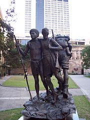 A bronze statue depicting a Papuan man assisting a wounded soldier down a muddy track while another soldier advances in the other direction