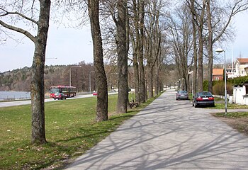 Ett okänt par på promenad längs Vårby allé, 1920-talet och samma plats i april 2012. I bakgrunden till vänster skymtar Mälaren, vy mot norr.