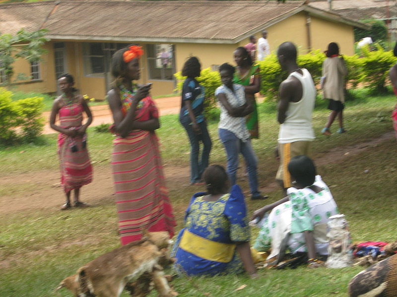 File:A girl in a kikooyi standing women in a gomesi seated.JPG