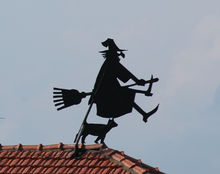 Une sorcière sur un balai avec un chat noir. Statue noire sur un toit.