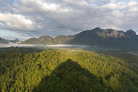 Conical shadow of Mount Nam Xay over green trees at golden hour, South-West view from the top, Vang Vieng, Laos