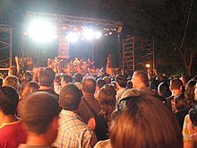 espectadores em pé assistindo a um show que acontece à noite