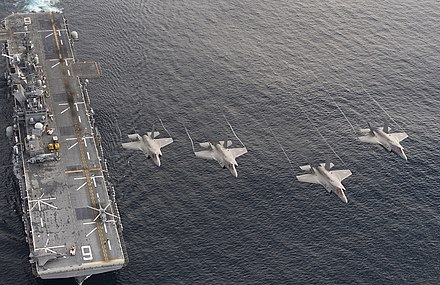Four Marine Corps F-35B Lightning II stealth fighters flying over the USS America (LHA-6)