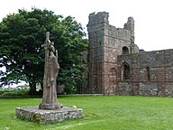 Statue av Aidan ved Lindisfarne klosterruinar.