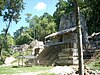 A small stepped pyramid flanked by the ruins of other stepped pyramids against a forest backdrop.