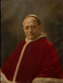 Portrait d'un homme portant des lunettes, coiffé d'une calotte blanche et portant une soutane blanche et une mosette rouge.