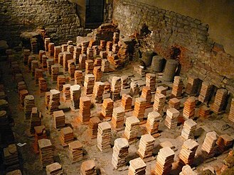 Caldarium. The room uses Roman hypocausts; a floor would have been supported by these structures, where hot air would circulate beneath and heat the room.