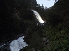 Chute d'eau illuminée au crépuscule avec le pont suspendu à l'arrière-plan.