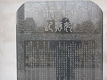 Fotografie horní půle kamenné desky ve vitríně s čínským nápisem.
