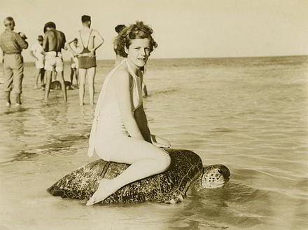 Young woman riding on the back of a turtle at Mon Repos Beach, near Bundaberg, ca. 1930.