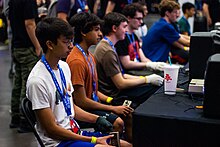 Seven male classic Tetris players sitting at a shared desk playing