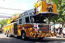 A modern Rosenbauer ladder truck in a unique "chrome yellow" livery at a parade.
