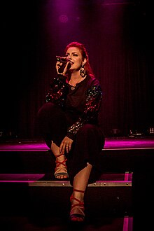 A woman sits on a stage using a microphone